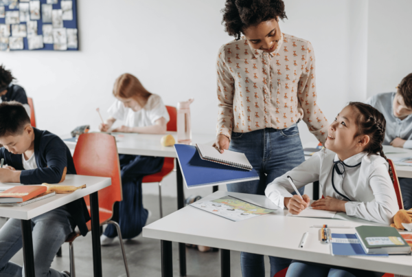 Teacher helping her students in an article about teachers getting unemployment during the summer